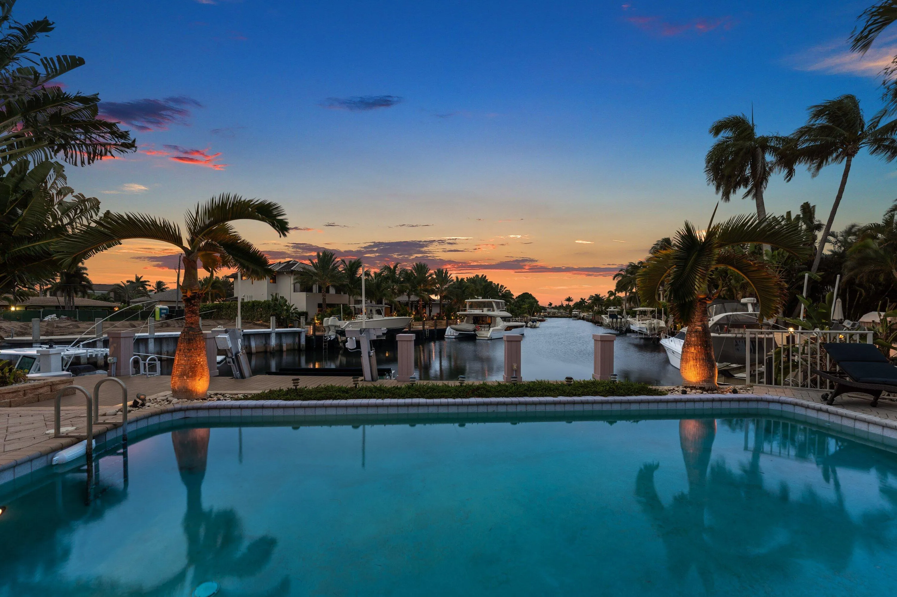 Waterfront property featuring a private swimming pool with integrated steps, a brick paver pool deck, and mature palm trees