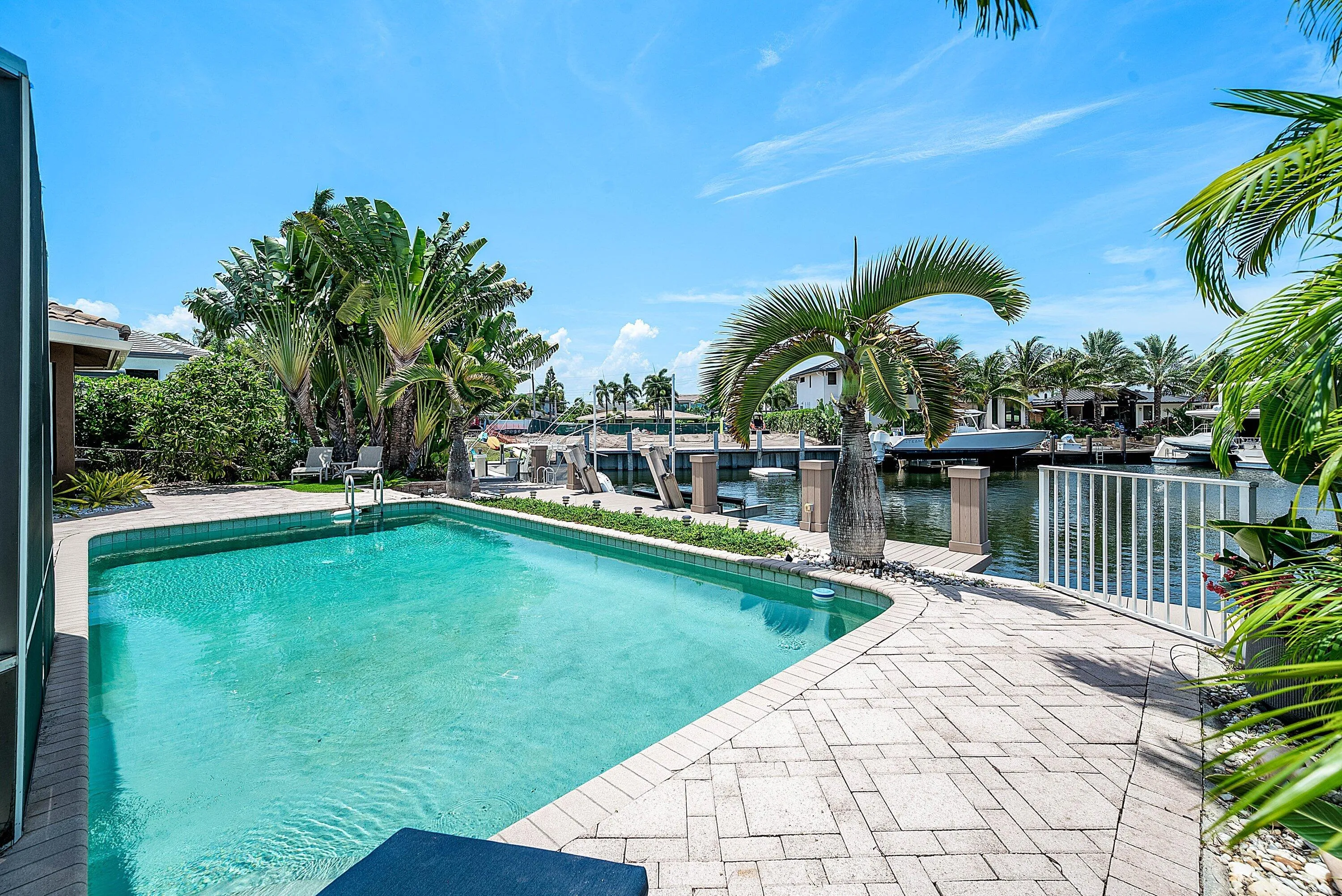 Waterfront property featuring a private swimming pool with integrated steps, a paver patio, lush tropical landscaping, and a private dock
