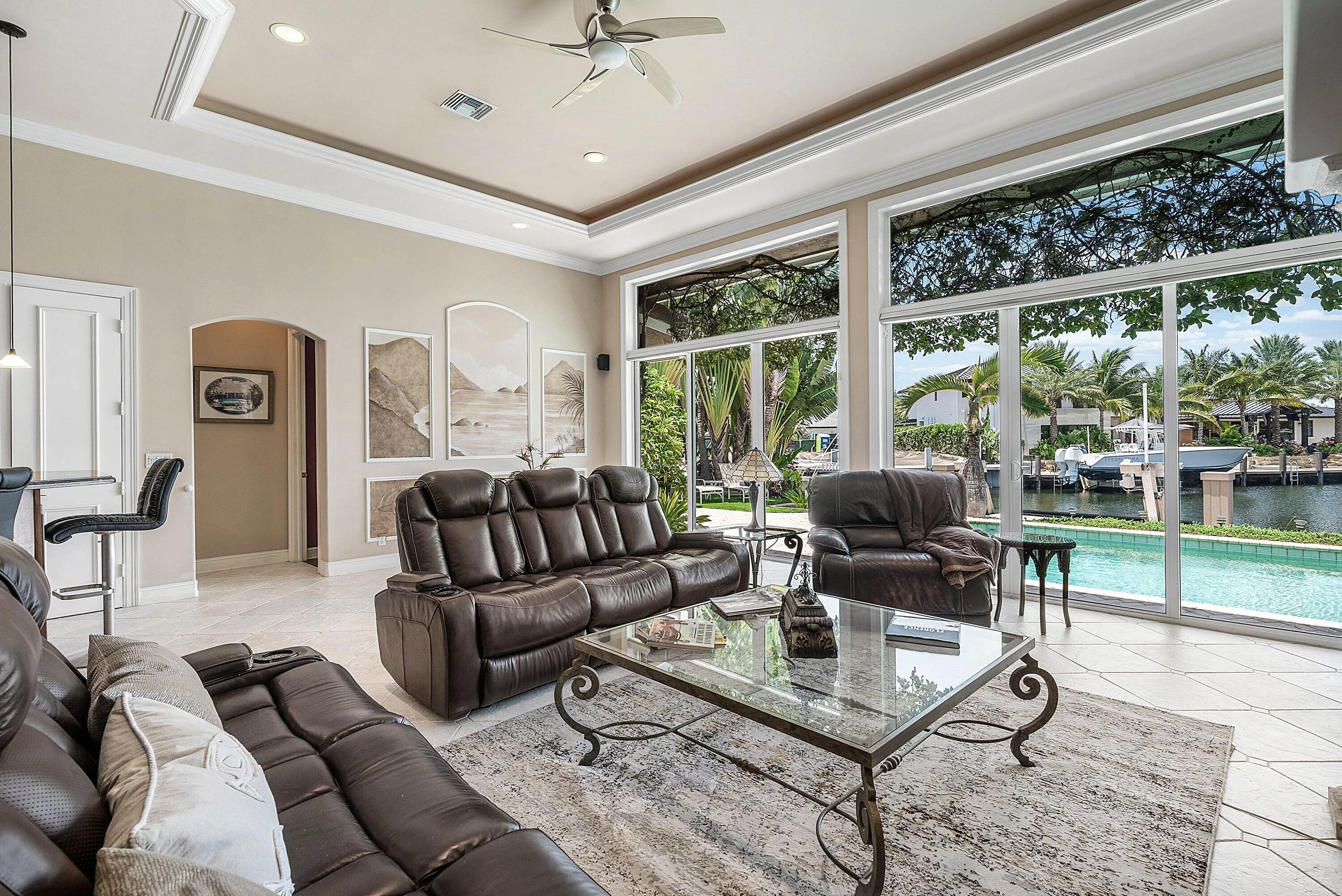 Spacious living area featuring floor-to-ceiling sliding glass doors, tray ceiling with recessed lighting, tile flooring, and a ceiling fan