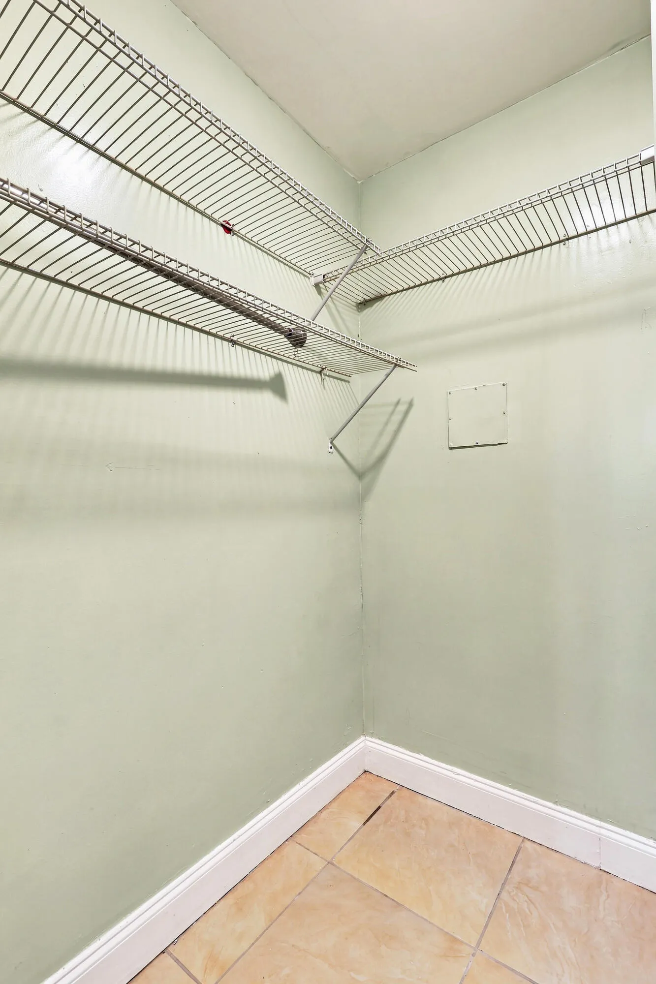 Corner closet featuring wire shelving and a hanging rod, tile flooring, and light green walls