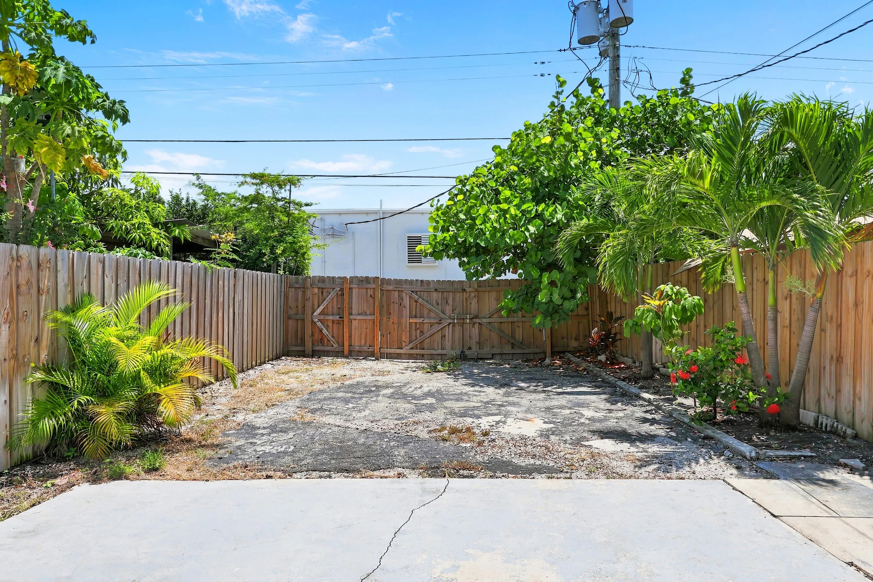 Private outdoor space featuring a wood fence perimeter, a double gate, mature trees, and a concrete patio pad