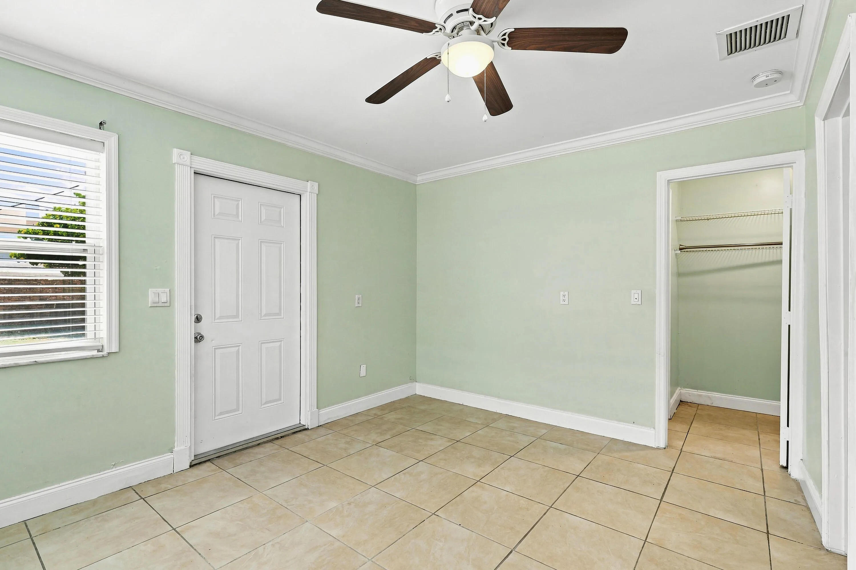 Interior space featuring tile flooring, a ceiling fan, a window with blinds, a paneled door, and an open closet with shelving