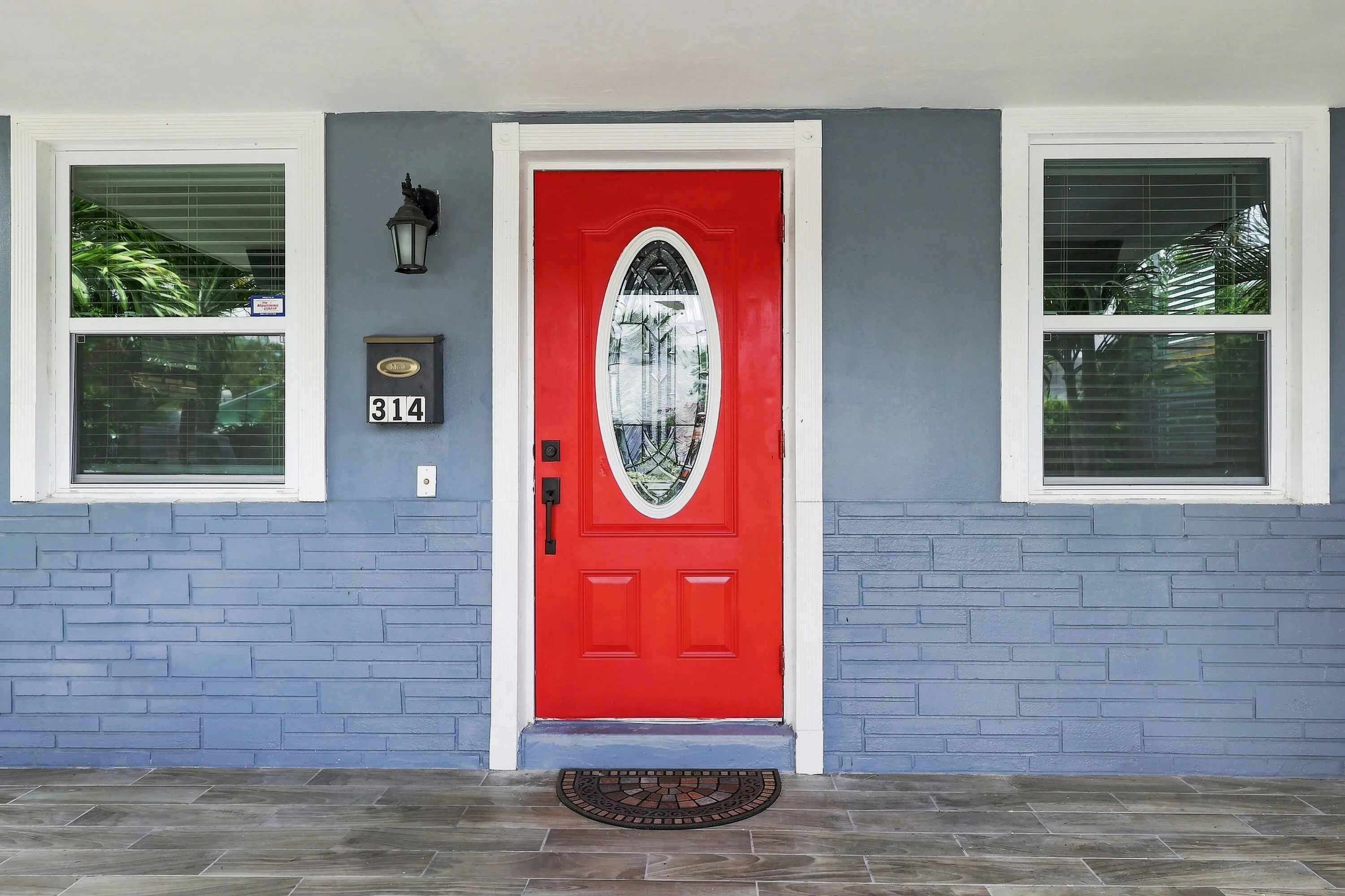 Vibrant red entry door with an oval decorative glass insert, flanked by two single-hung windows with white trim