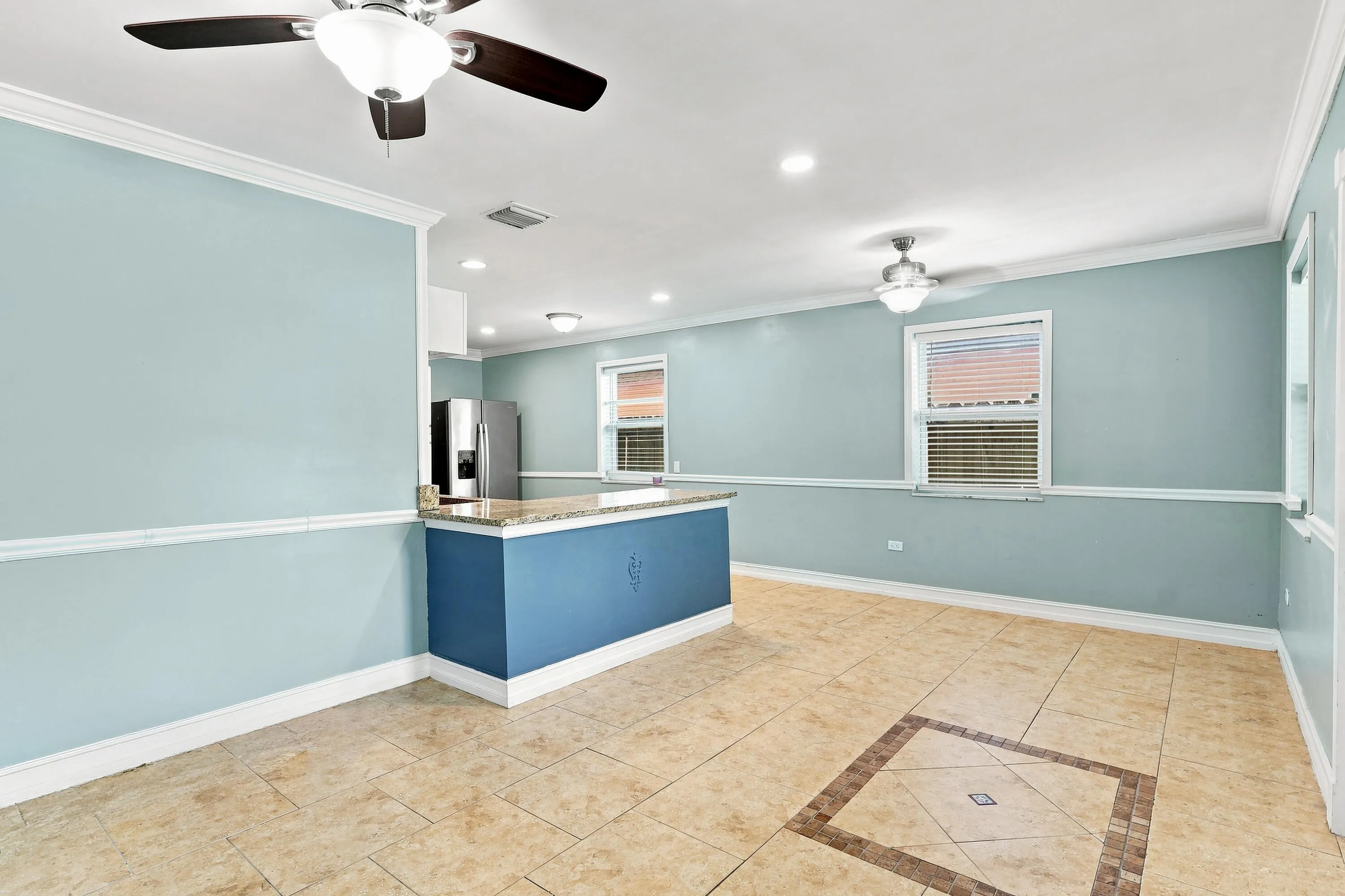 Open concept living space featuring tile flooring with a decorative inlay, two ceiling fans, recessed lighting, and a kitchen island with a stone-finish countertop