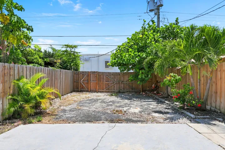 Private outdoor space featuring a wood fence perimeter, a double gate, mature trees, and a concrete patio pad