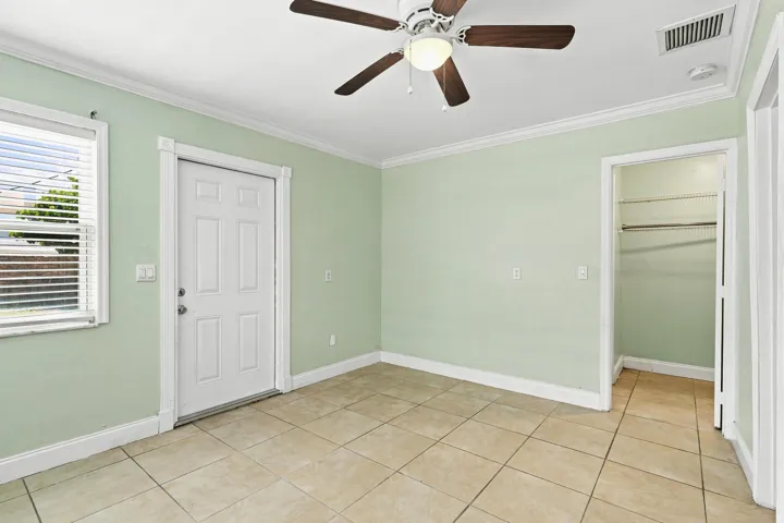 Interior space featuring tile flooring, a ceiling fan, a window with blinds, a paneled door, and an open closet with shelving