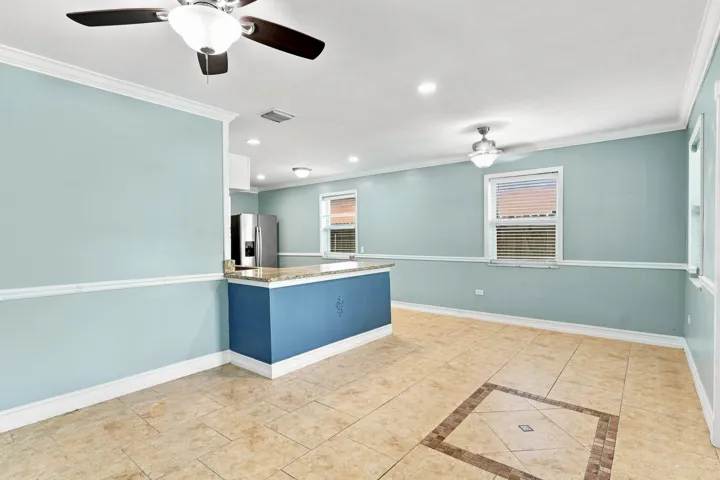 Open concept living space featuring tile flooring with a decorative inlay, two ceiling fans, recessed lighting, and a kitchen island with a stone-finish countertop