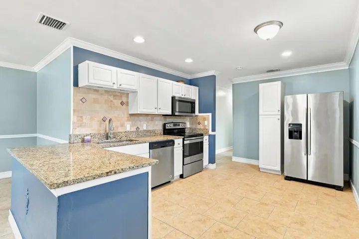 Kitchen featuring granite countertops, stainless steel appliances, white cabinetry, and a tile backsplash with decorative inlays