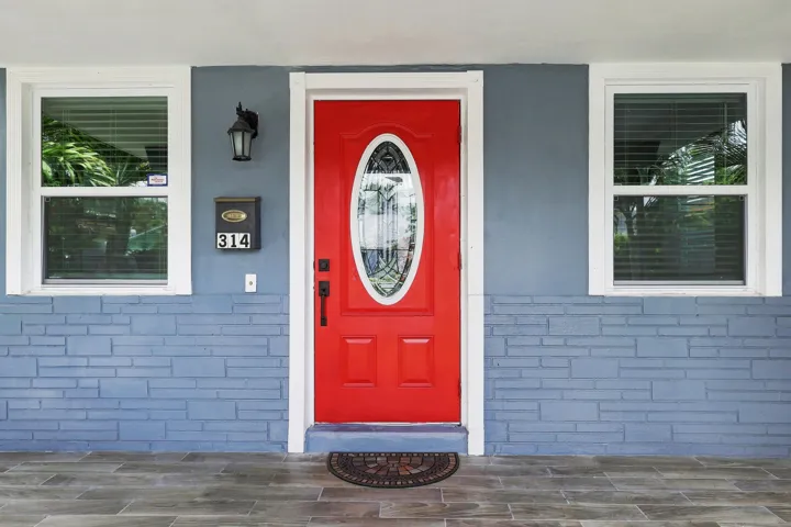 Vibrant red entry door with an oval decorative glass insert, flanked by two single-hung windows with white trim