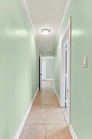 Hallway featuring tile flooring, light green walls, white crown molding, and recessed lighting
