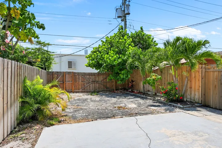 Enclosed backyard area featuring a wooden privacy fence, a concrete patio, and a variety of mature trees and tropical plantings