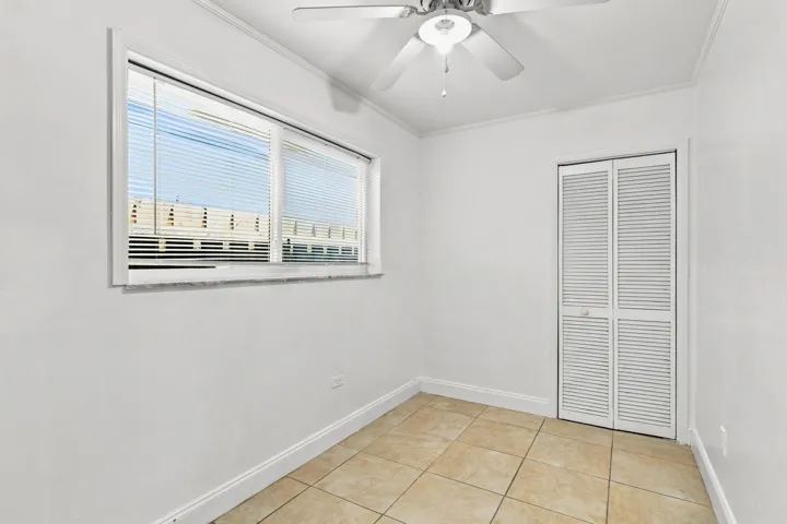 Room featuring a window with blinds, bi-fold louvered closet doors, a ceiling fan with integrated lighting, and tile flooring