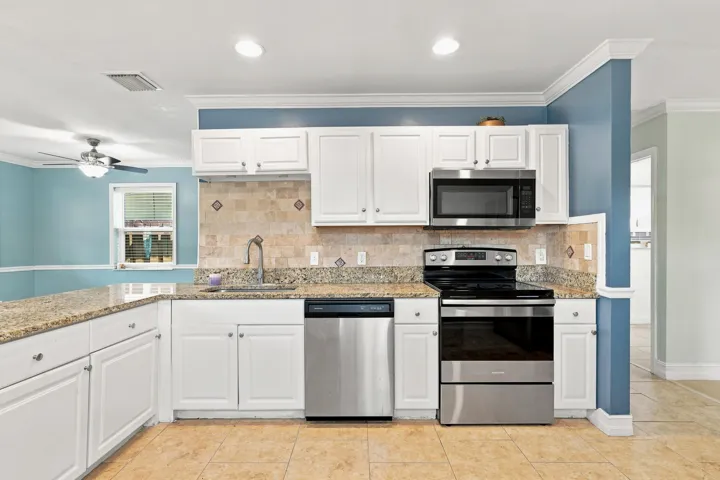 Kitchen featuring white shaker-style cabinetry, a granite-finish countertop, stainless steel appliances, a tiled backsplash with decorative accents, and tile flooring