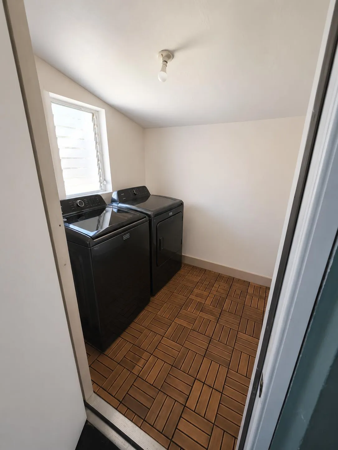 Dedicated laundry area featuring wood-finish tile flooring and a louvered window
