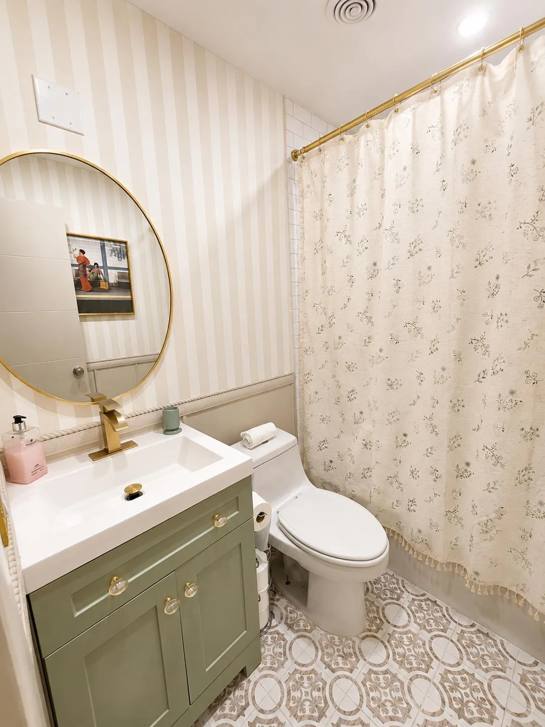 Bathroom featuring a sage green vanity with gold hardware, a circular gold-framed mirror, a modern white toilet, patterned floor tiling, and striped wallpaper