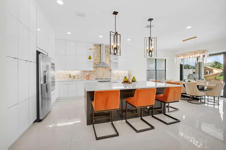 Modern kitchen featuring an expansive center island with seating, high-gloss white cabinetry, and stainless steel appliances