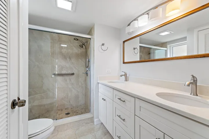 Renovated bath with a walk-in glass shower and natural stone tile