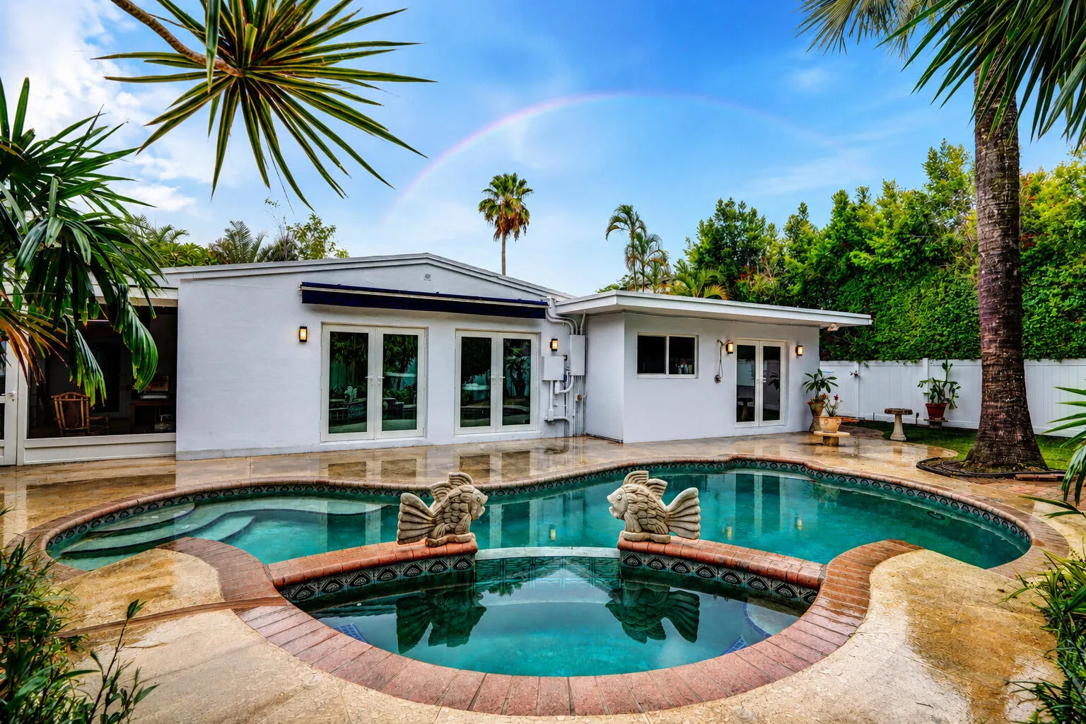 Tropical backyard with pool and spa, surrounded with privacy fencing.