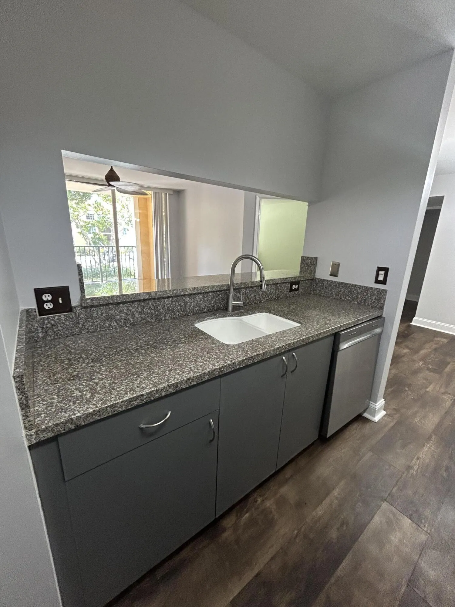 Kitchen counter with granite-finish countertops, undermount sink, gooseneck faucet, and dark wood-finish flooring