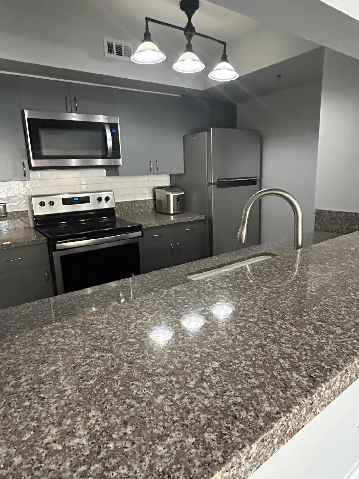 Kitchen featuring speckled stone countertops, stainless steel appliances, grey cabinetry, and a subway tile backsplash