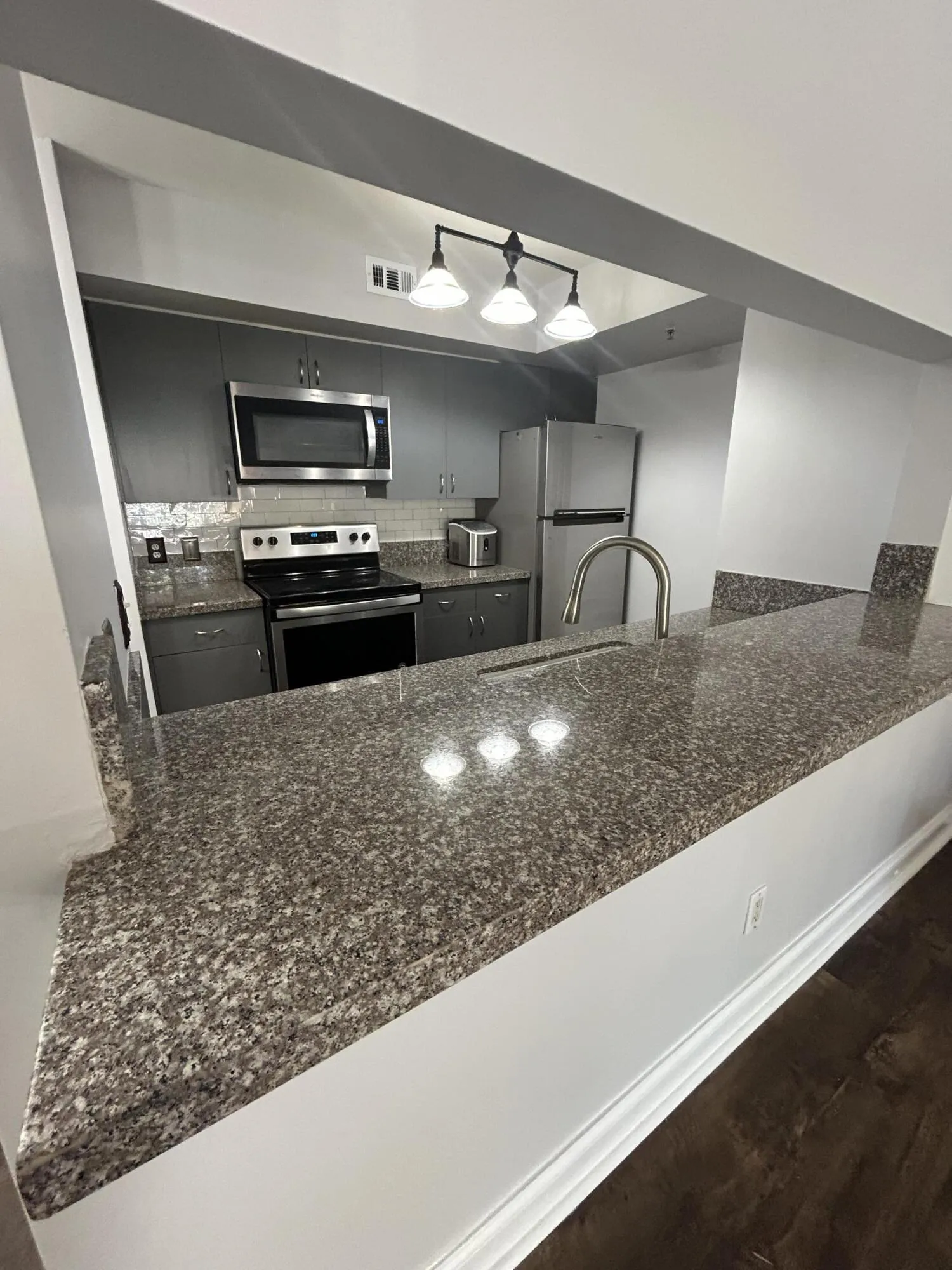 Kitchen featuring an extended granite countertop, stainless steel appliances, dark wood-finish flooring, recessed lighting, and a tile backsplash