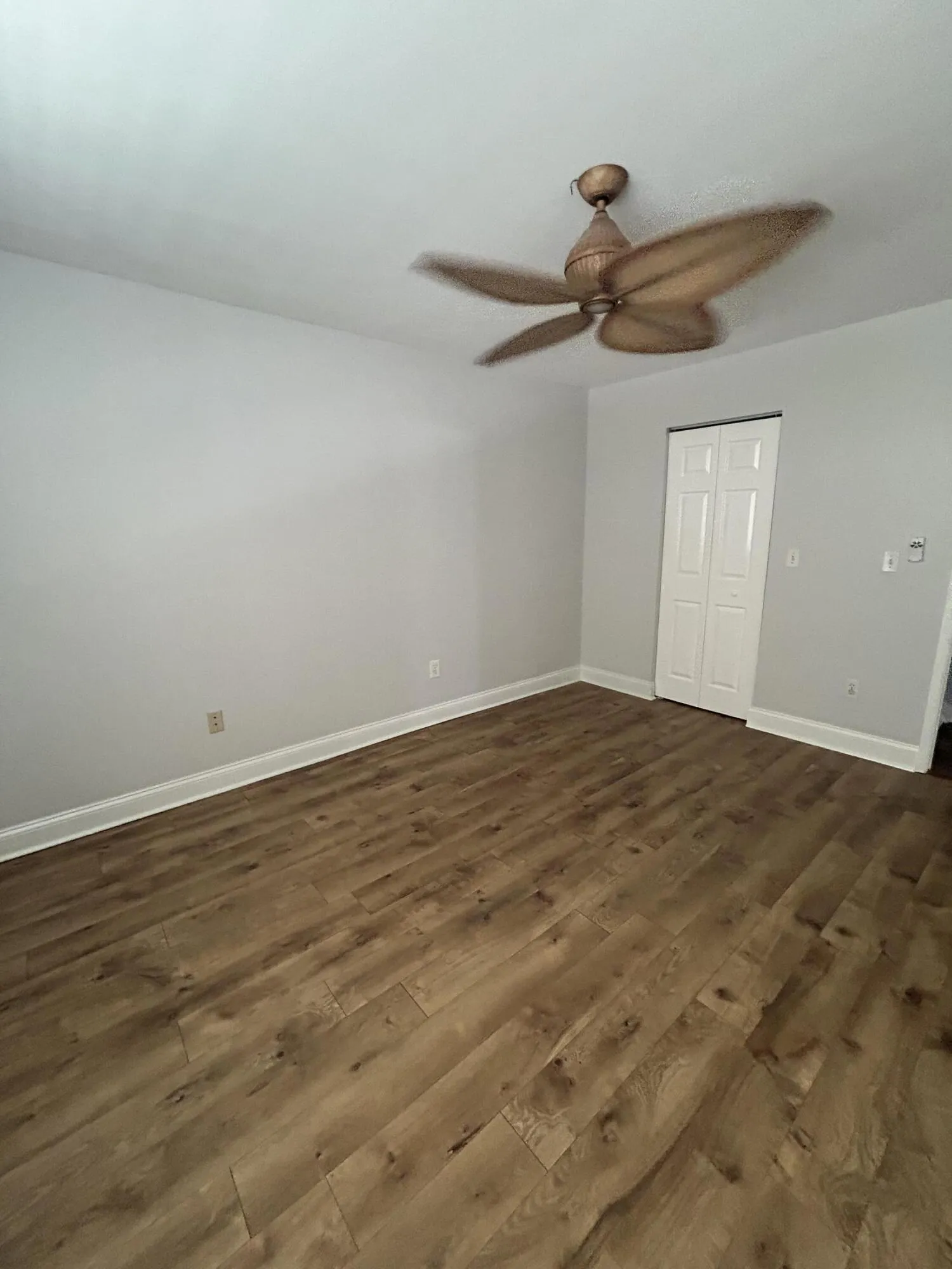 Spacious room featuring wood-finish flooring, white baseboards, and a ceiling fan