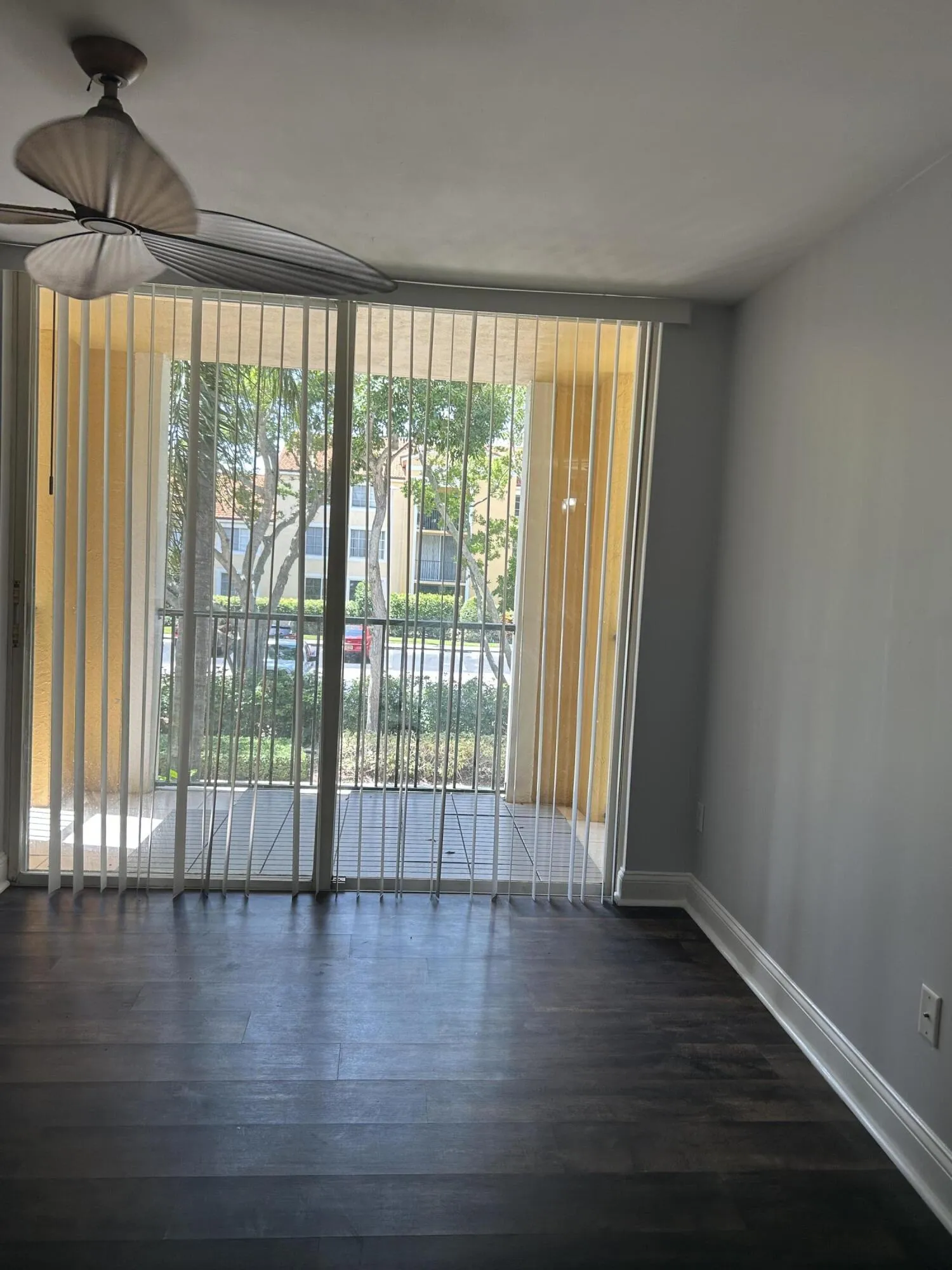 Spacious room featuring dark wood-finish flooring, a ceiling fan, and a balcony with vertical blinds