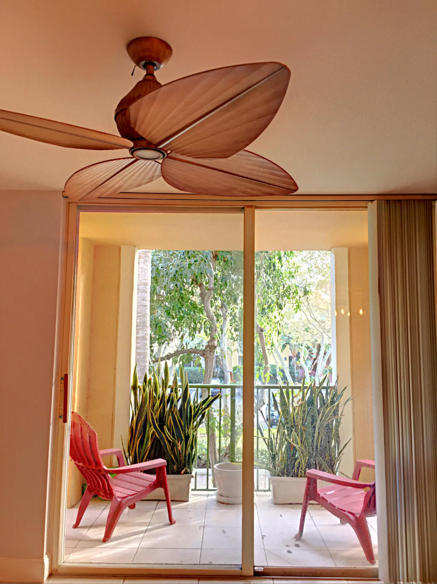 Sliding glass doors opening to a tiled balcony with a metal railing and mature tree foliage