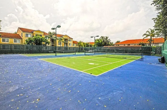 Dual tennis courts featuring blue and green surfaces, perimeter fencing, and overhead lighting