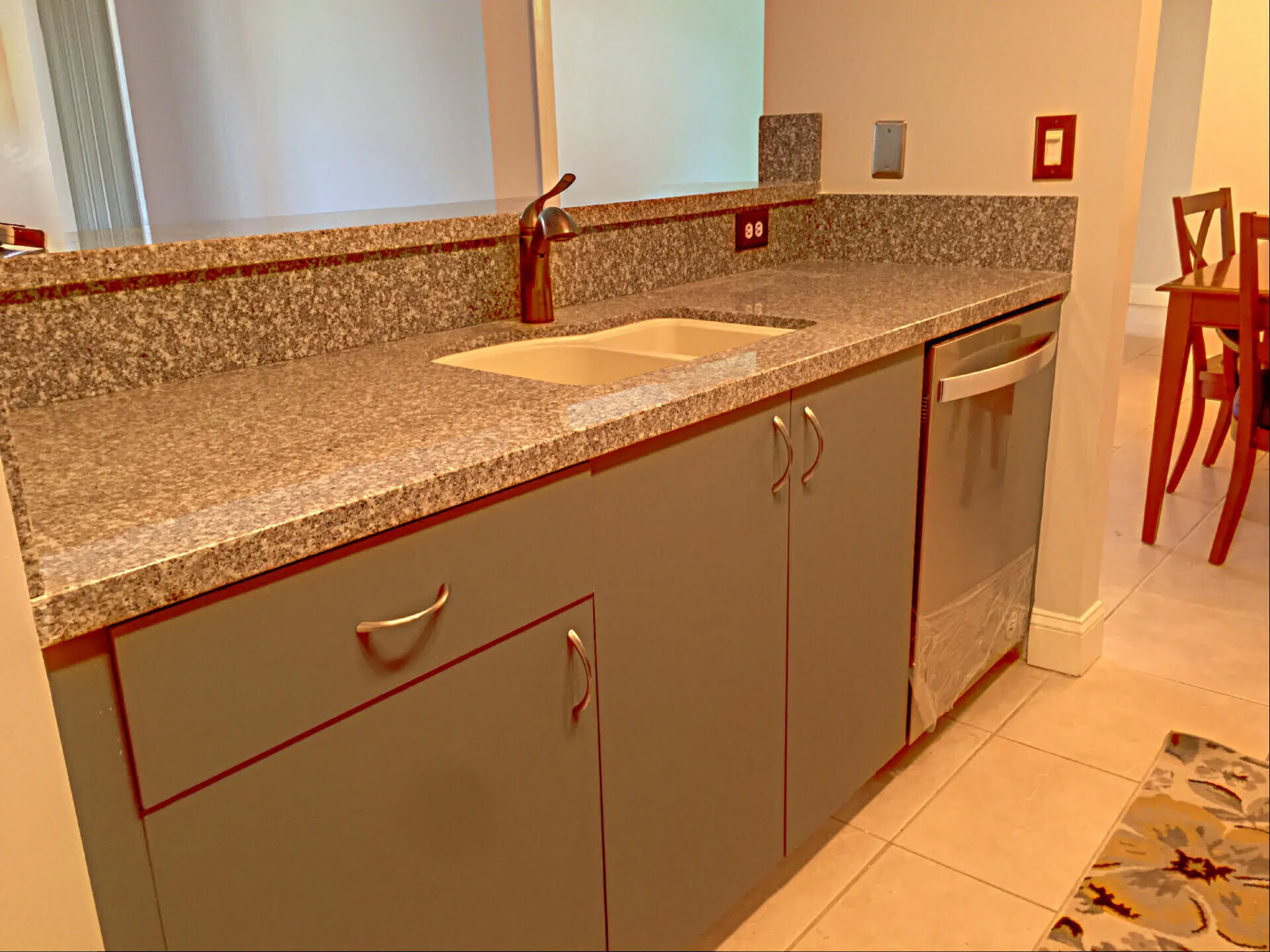 Kitchen counter space featuring granite countertops with integrated backsplash, a double basin sink, a brushed nickel faucet, light gray cabinetry, and a stainless steel dishwasher
