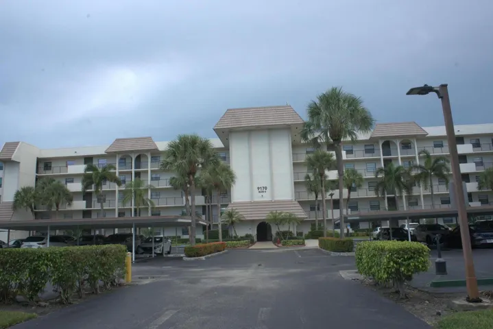 Multi-story residential building with multiple balconies, covered parking, and palm trees
