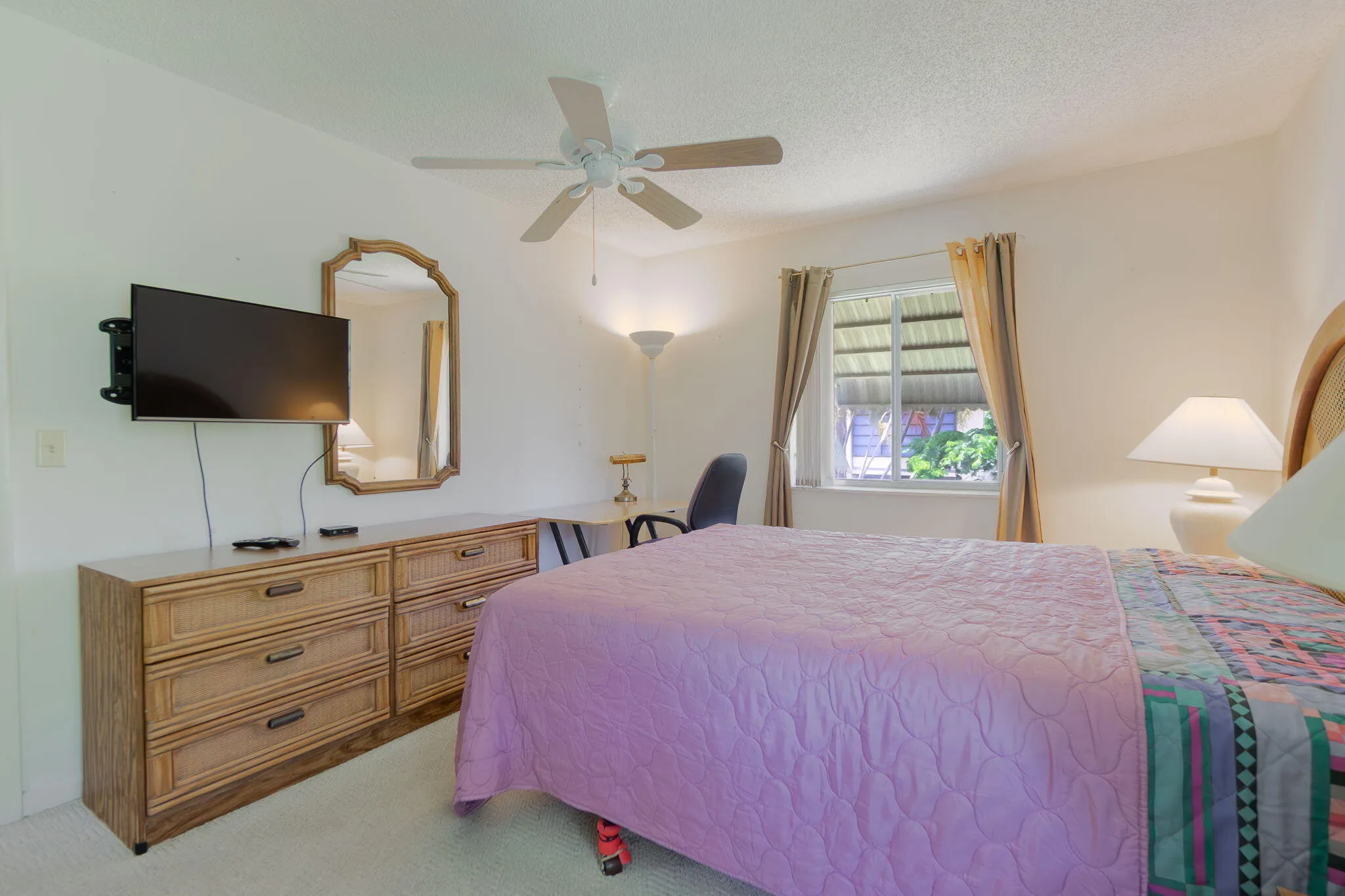 Bedroom featuring a window with exterior louvered blinds, a ceiling fan, and wall-mounted television