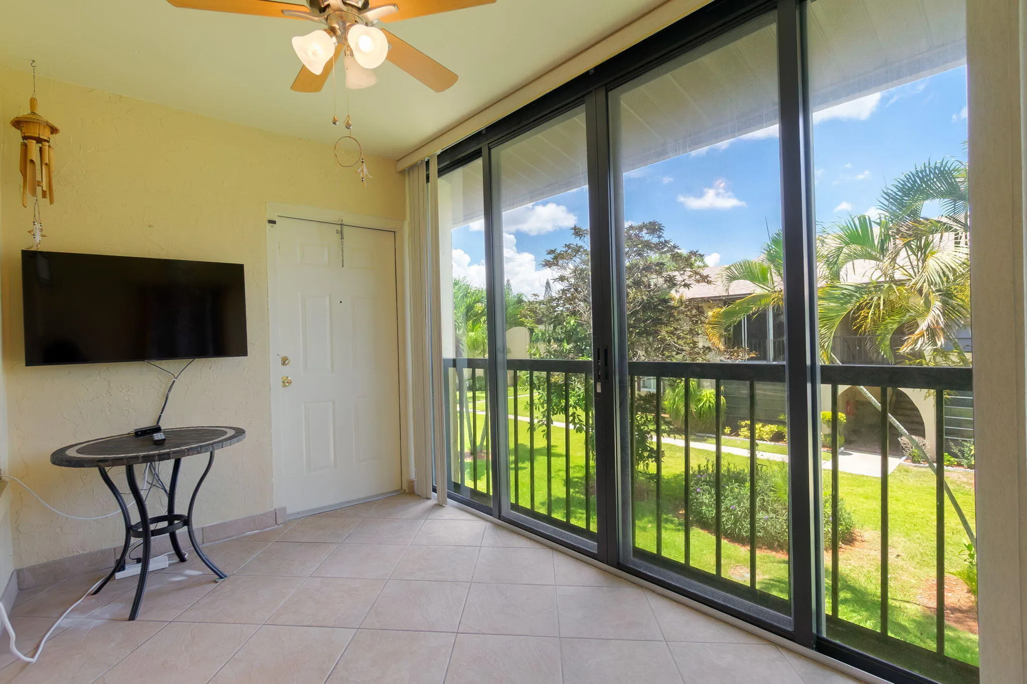 Enclosed patio area featuring large impact sliding glass doors, tile flooring, a ceiling fan, and a view of green landscaping