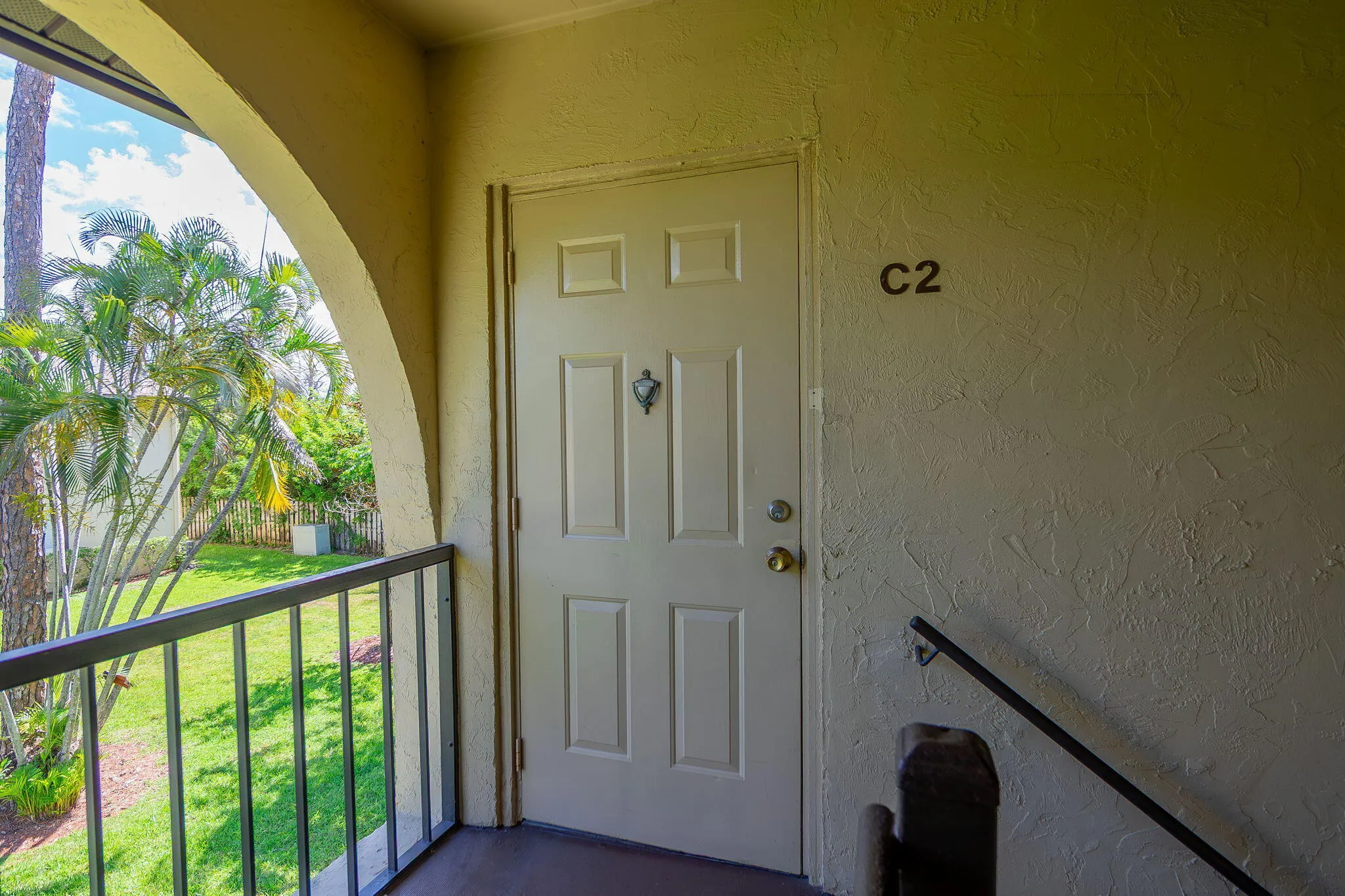 Entryway featuring a paneled door with brass hardware, stucco exterior, and an arched architectural opening