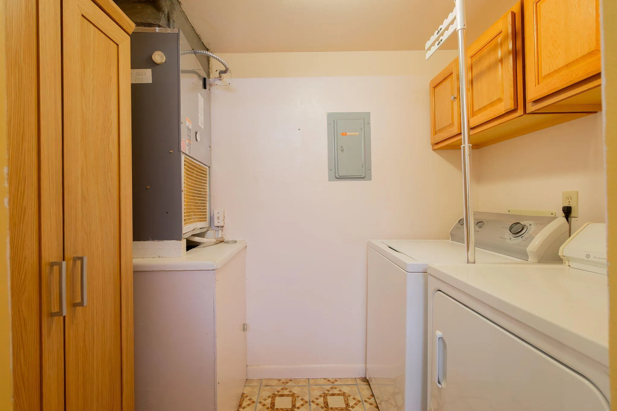 Dedicated utility space featuring light wood-finish cabinetry, a built-in countertop, and patterned floor tiling