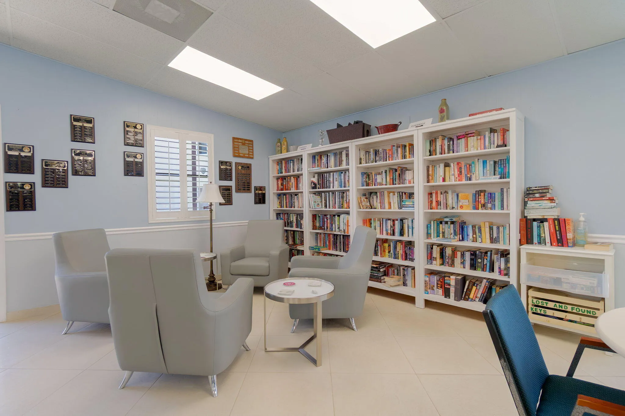Library space featuring built-in white shelving, light blue walls, and a window with white louvered shutters