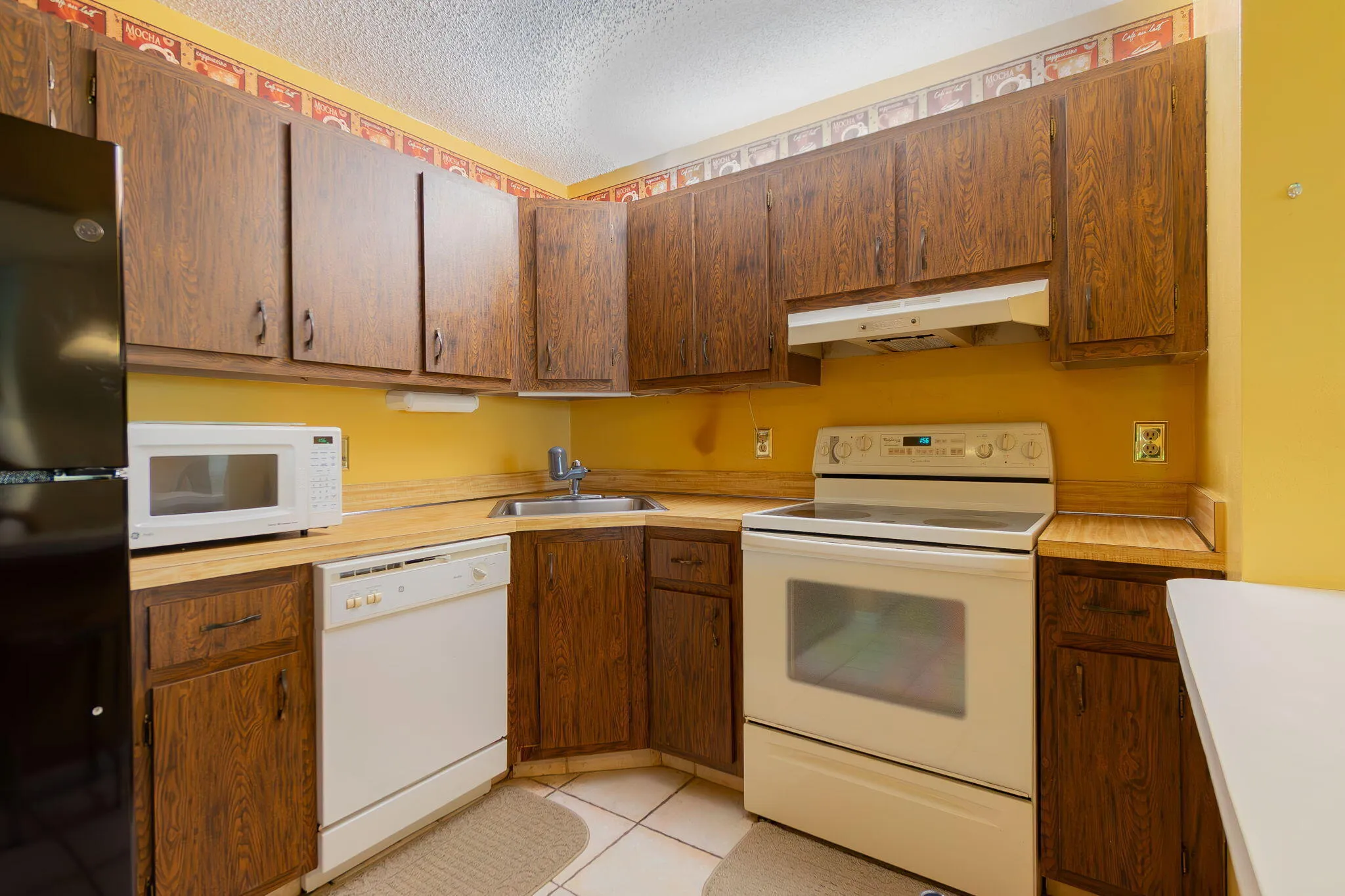 Kitchen featuring wood-finish cabinetry, solid surface countertops, and white tile flooring