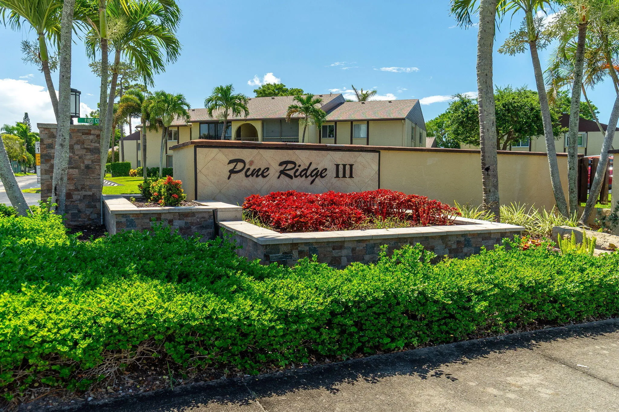 Stone-clad monument signage introducing Pine Ridge III, framed by lush green shrubs and vibrant red foliage