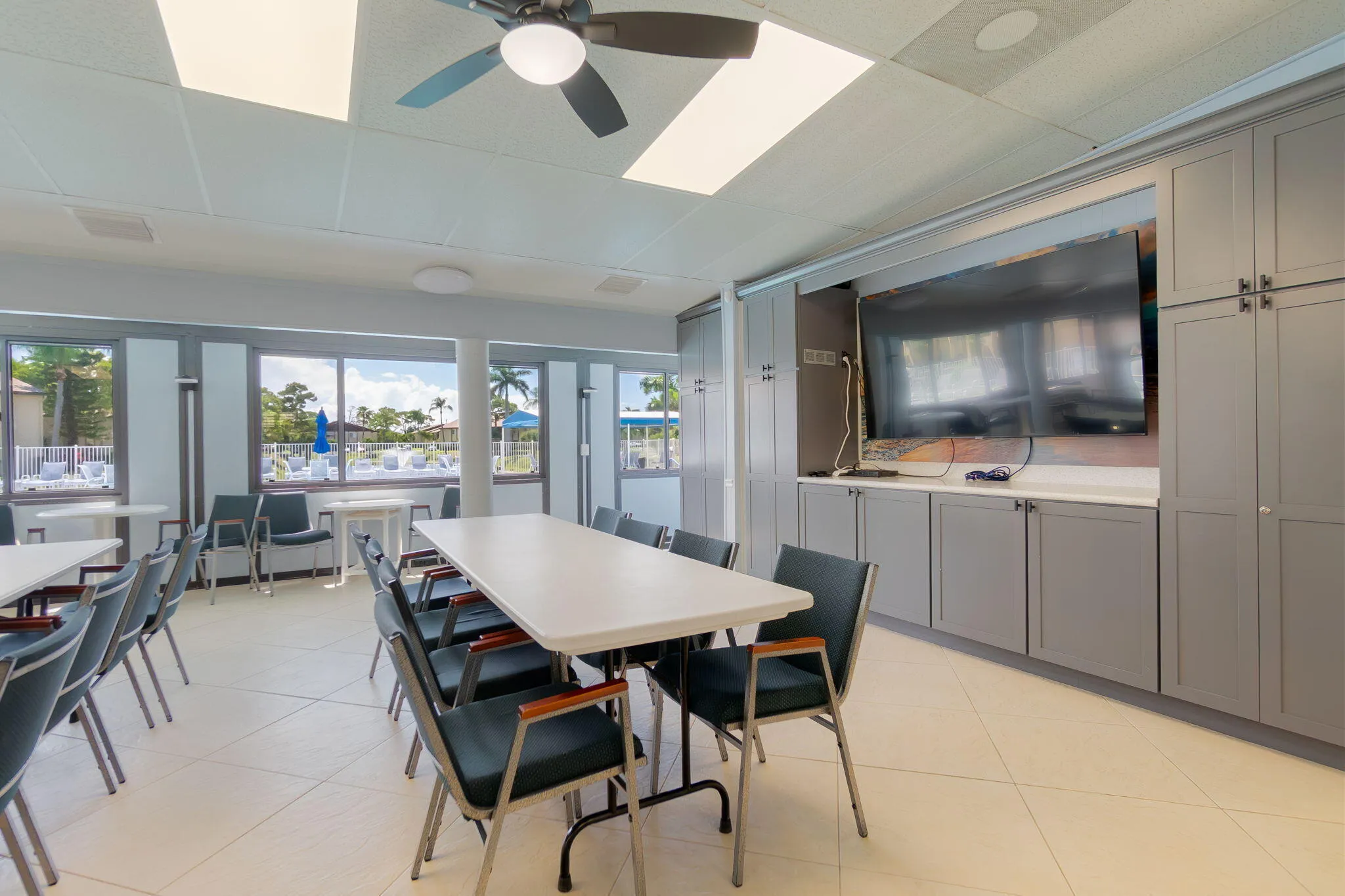 Spacious room featuring multiple tables and chairs, large windows, a ceiling fan, and built-in cabinetry with an integrated television