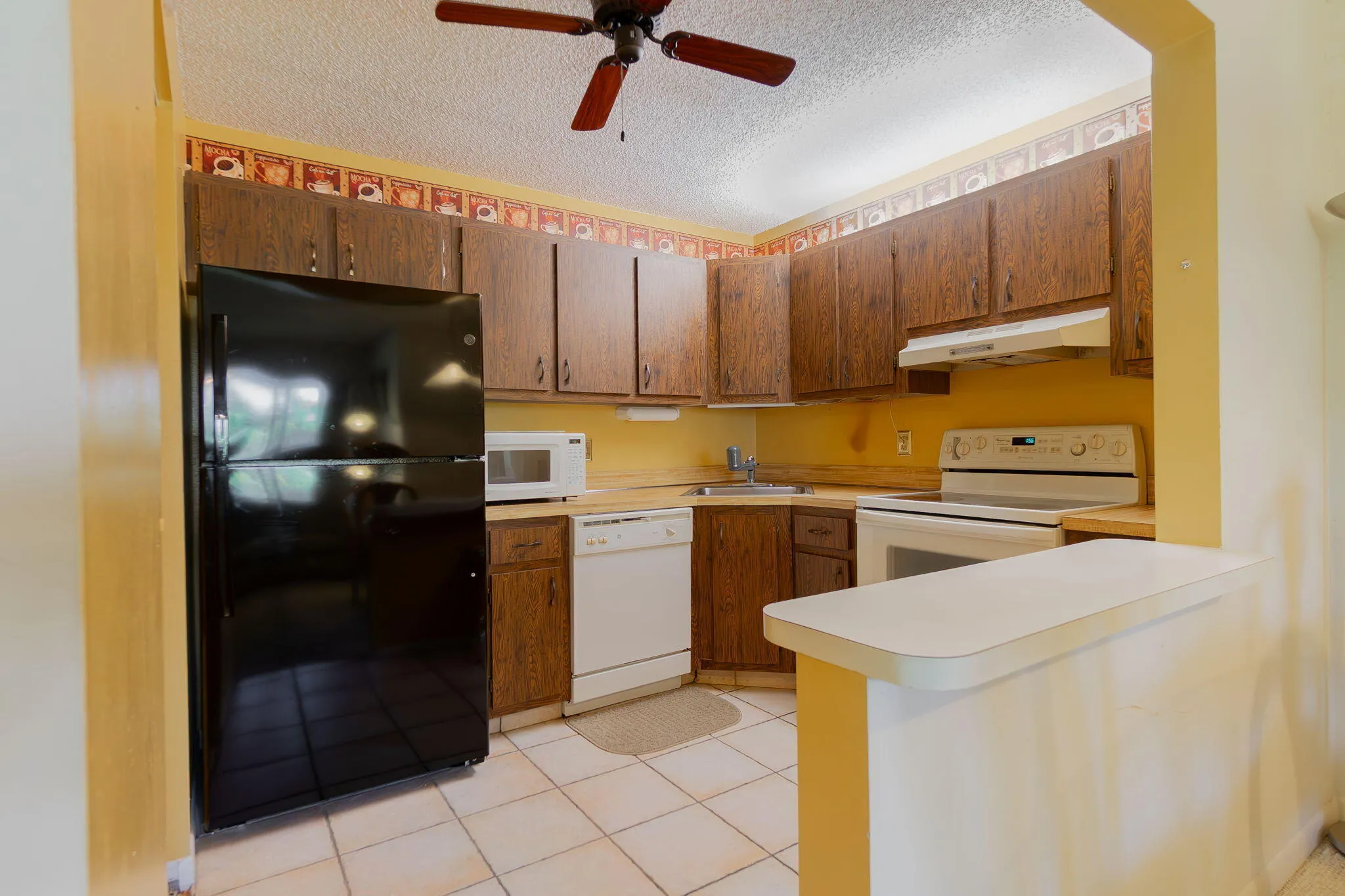 U-shaped kitchen featuring wood-finish cabinetry, white tile flooring, and a ceiling fan with wood-finish blades