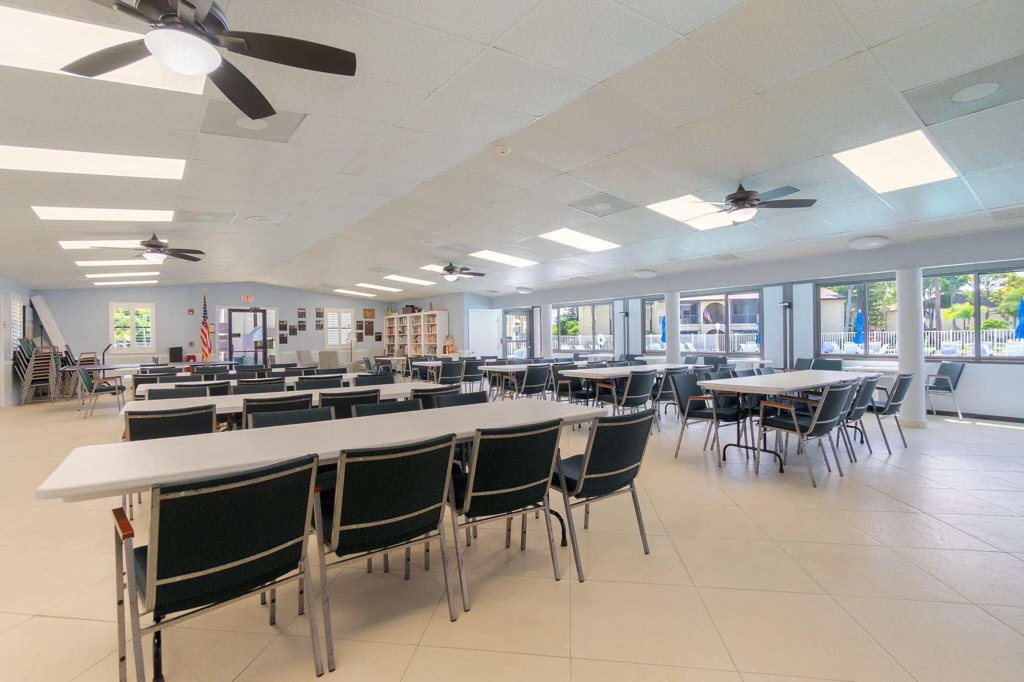 Spacious common room featuring light-colored tile flooring, multiple ceiling fans, recessed lighting, and expansive windows