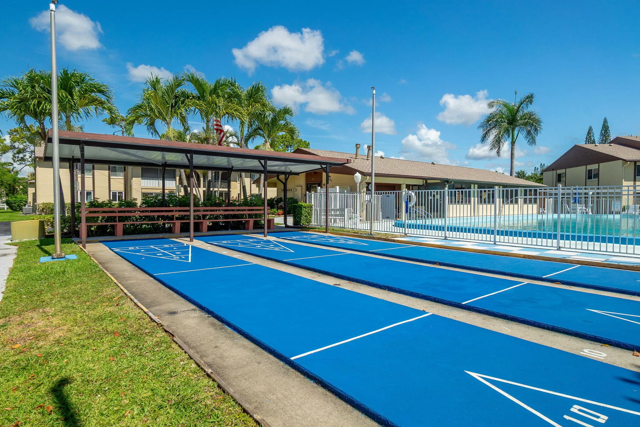Outdoor shuffleboard courts with bright blue surfacing, accompanied by a covered seating area