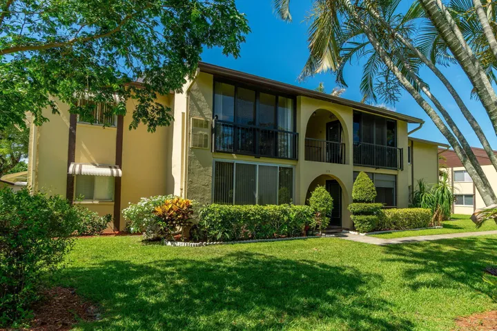 Two-story stucco exterior featuring screened balconies with black railings, arched entryways, and mature landscaping