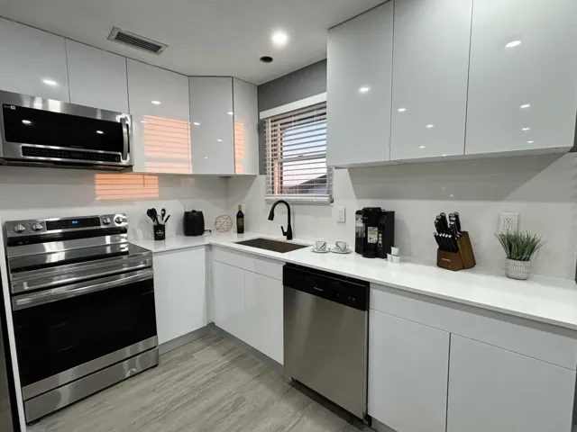 Contemporary kitchen featuring white flat-panel cabinetry, stainless steel appliances, a black sink, and a black faucet
