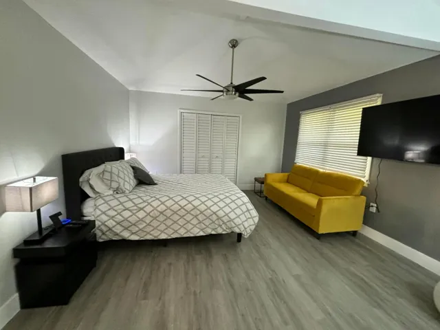 Vaulted ceiling with a contemporary ceiling fan, wood-finish flooring, louvered closet doors, and horizontal blinds