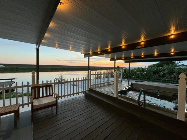 Covered deck featuring a built-in hot tub, dark wood-finish flooring, and a white picket fence