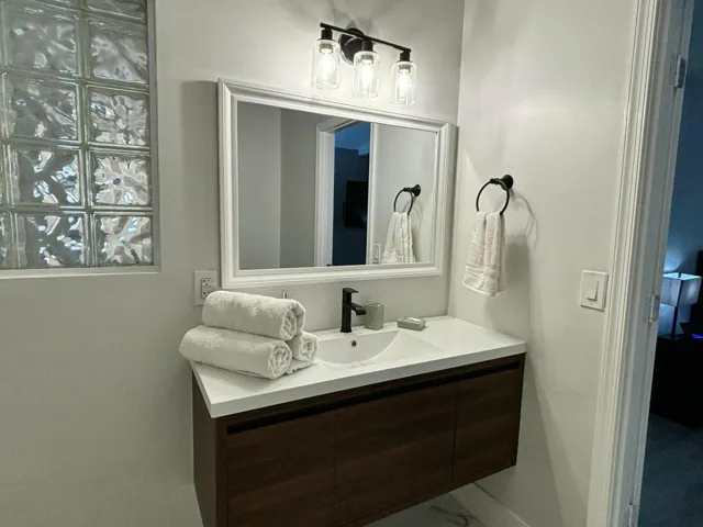 Bathroom vanity featuring a floating wood-finish cabinet with white countertop, integrated sink, and black modern faucet