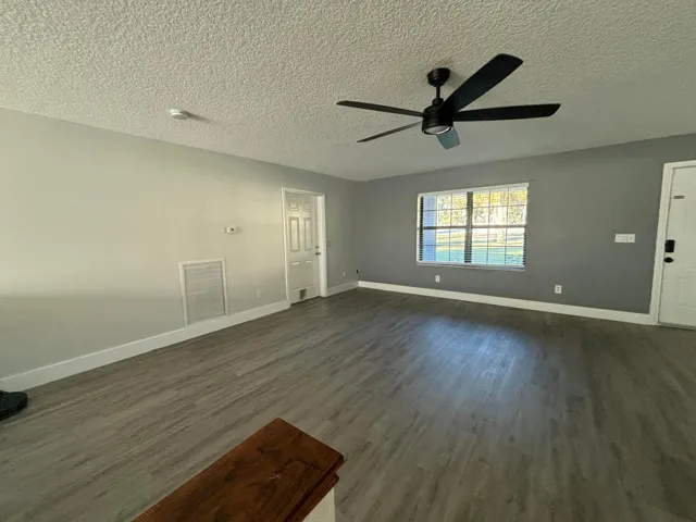 Spacious interior featuring wood-finish flooring, light grey walls, white baseboards, and a contemporary ceiling fan
