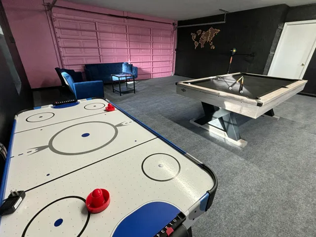Recreational space featuring air hockey and billiards tables, a textured pink garage door, and a light gray carpeted floor