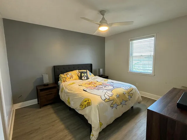 Bedroom featuring wood-finish flooring, a contemporary ceiling fan with integrated lighting, and a window equipped with blinds